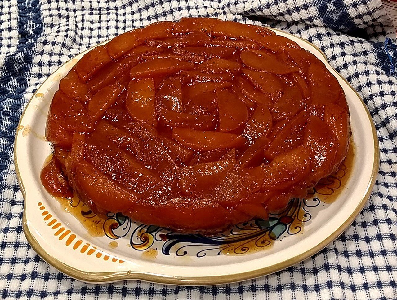 Tarte tatin inteira, com as maçãs caramelizadas por cima, num prato de cerâmica