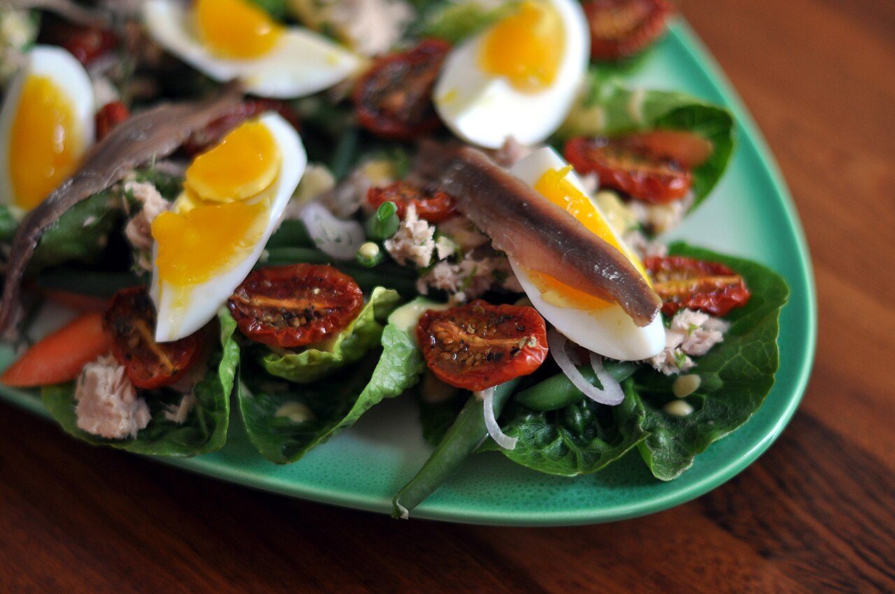 Salada niçoise com ovos cozidos em quartos, filés de anchova, tomates e folhas verdes numa travessa