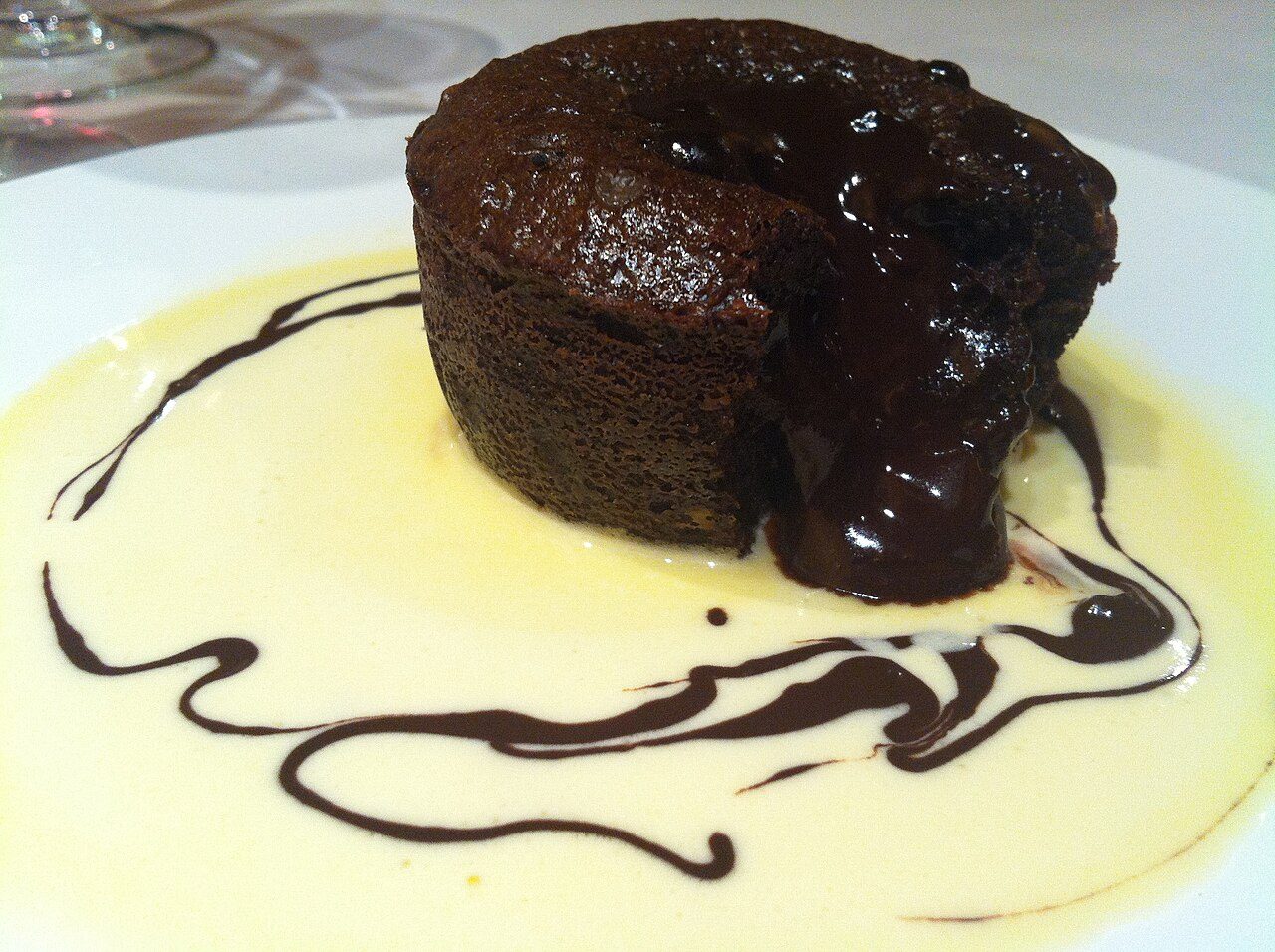 Petit gâteau de chocolate partido, com o centro líquido escorrendo sobre creme claro no prato