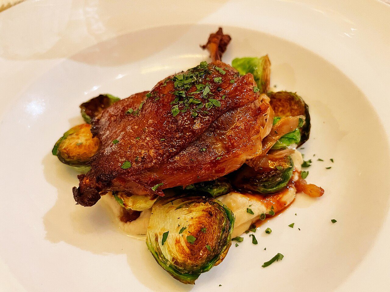 Coxa de confit de canard com a pele dourada servida sobre couves-de-bruxelas assadas