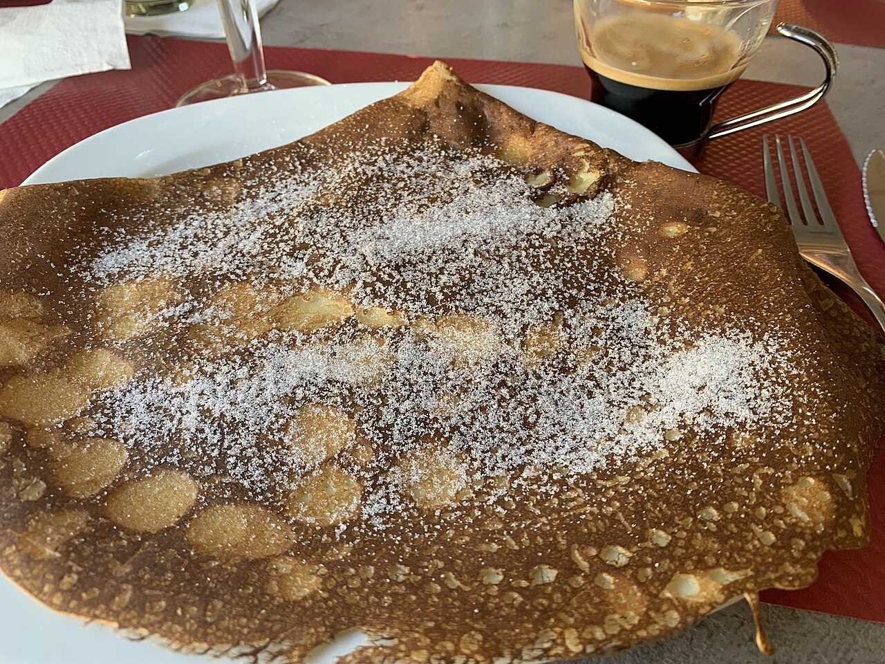 Crepe francês dobrada com açúcar polvilhado, servida num prato numa crêperie