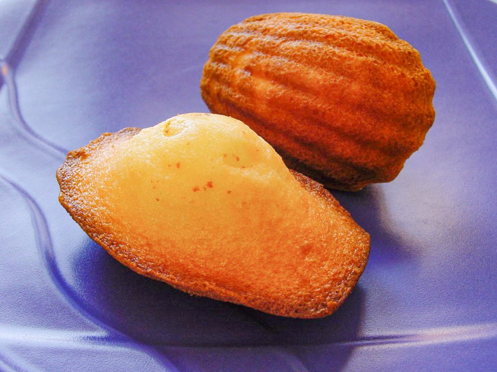 Duas madeleines de Commercy douradas, uma mostrando o lado liso e outra o lado estriado em forma de concha
