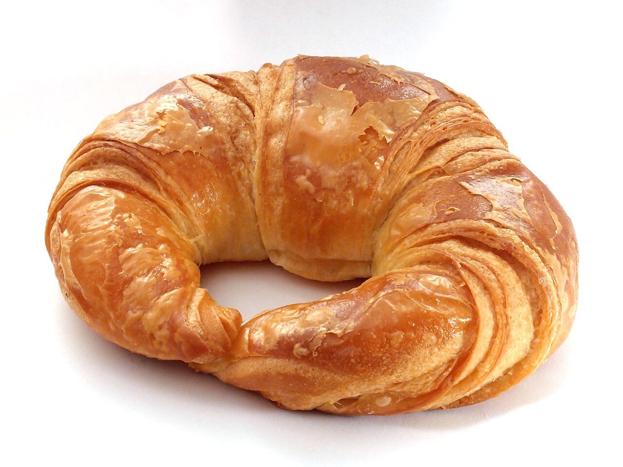 Croissant inteiro em meia-lua, dourado e brilhante, com as camadas de massa visíveis, sobre fundo branco