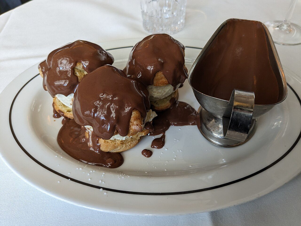Profiteroles cobertas de calda de chocolate com molheira de chocolate quente numa brasserie de Paris