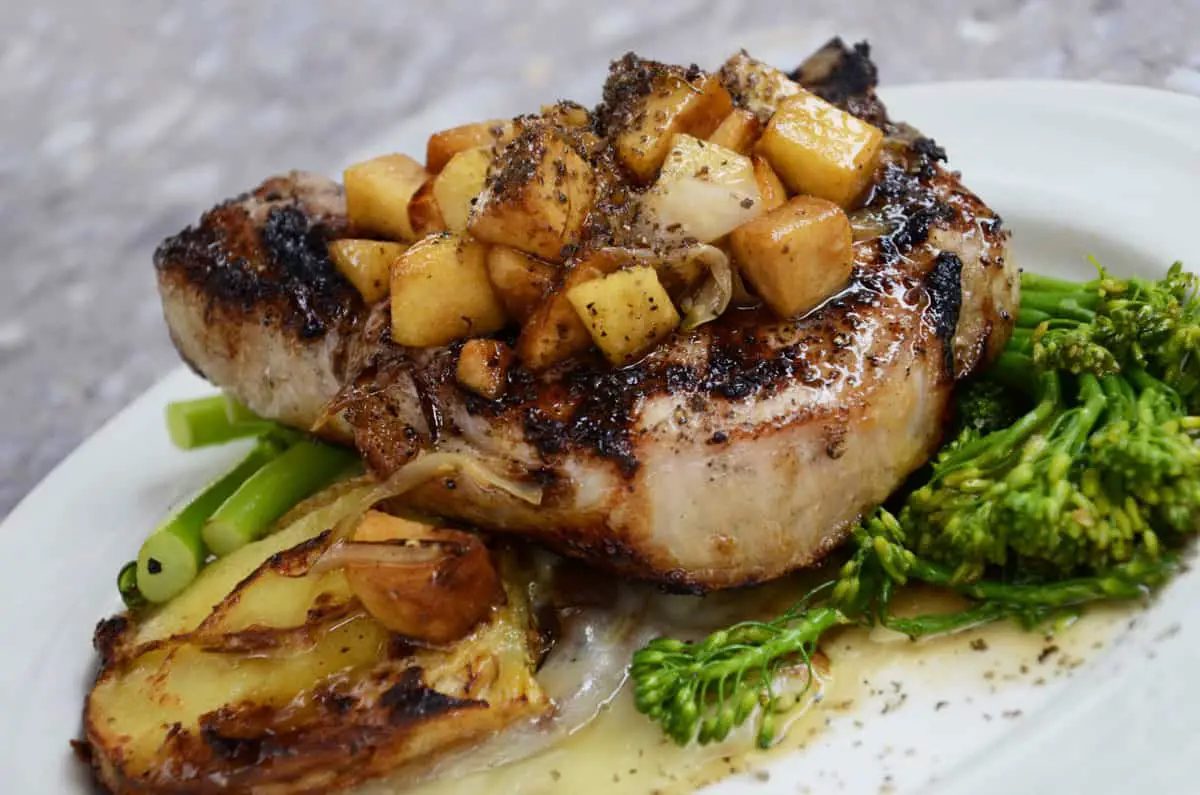 Bisteca de porco grelhada com cubos de maçã, brócolis e batata assada em prato branco