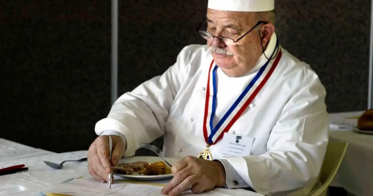Chef Pierre Troisgros com medalha de fita tricolor provando um prato e fazendo anotações